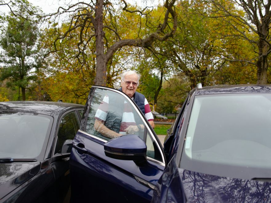 Ein älterer Herr steht an der geöffneten Tür eines Autos.