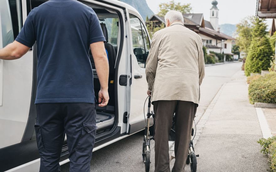 Ein Fahrer hält die Schiebetür auf, ein älterer Herr mit Rollator geht zum Wagen.