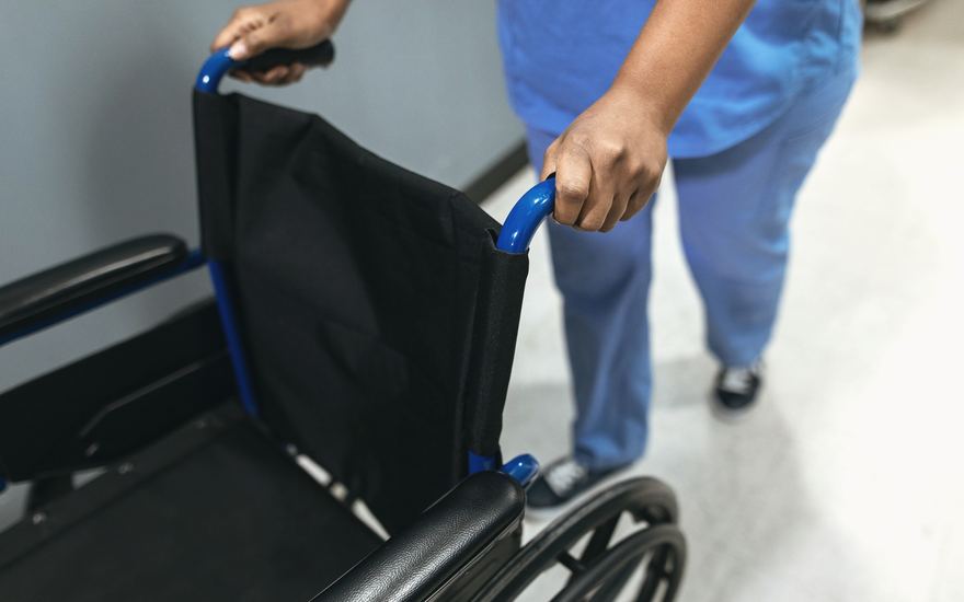 Ein Rollstuhl wird durch einen Klinikflur geschoben.