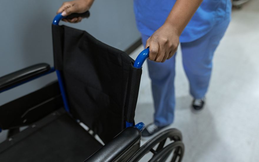 Ein Rollstuhl wird durch einen Klinikflur geschoben.