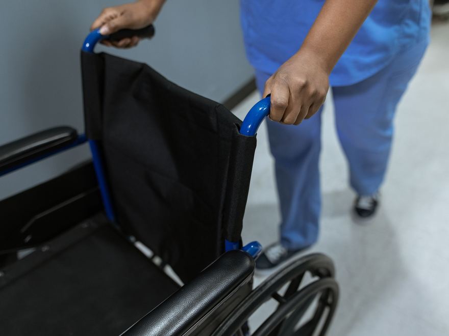Ein Rollstuhl wird durch einen Klinikflur geschoben.
