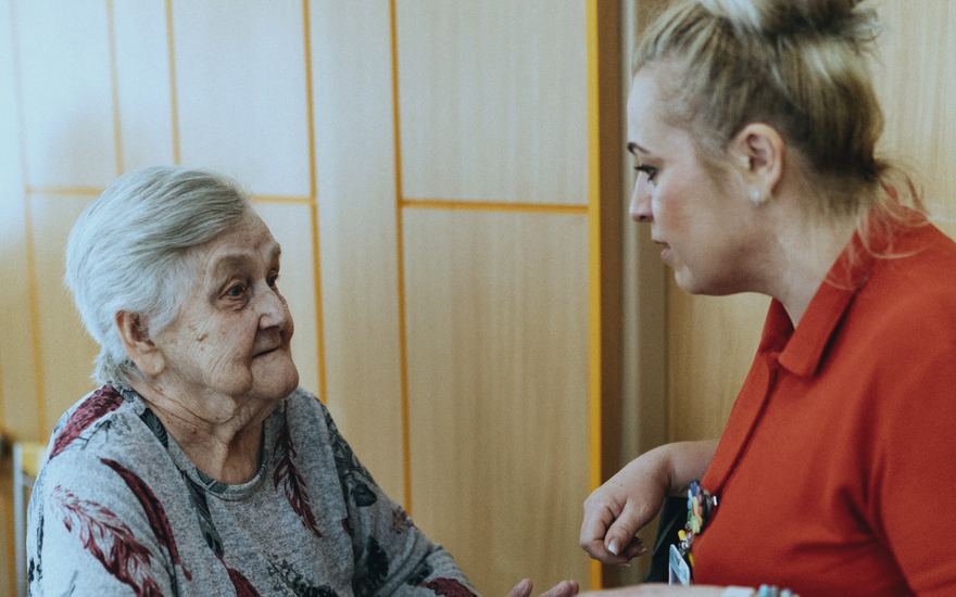 Eine Pflegerin begleitet eine ältere Dame über einen Flur.